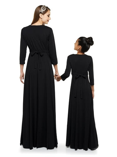Back view of adult and youth models wearing the Charlotte Heart Shaped Neck 3/4 Sleeve Dress in black, showcasing the tied waist detail and flowing full-length skirt, designed for choir concerts, formal performances, and coordinated group ensembles.
